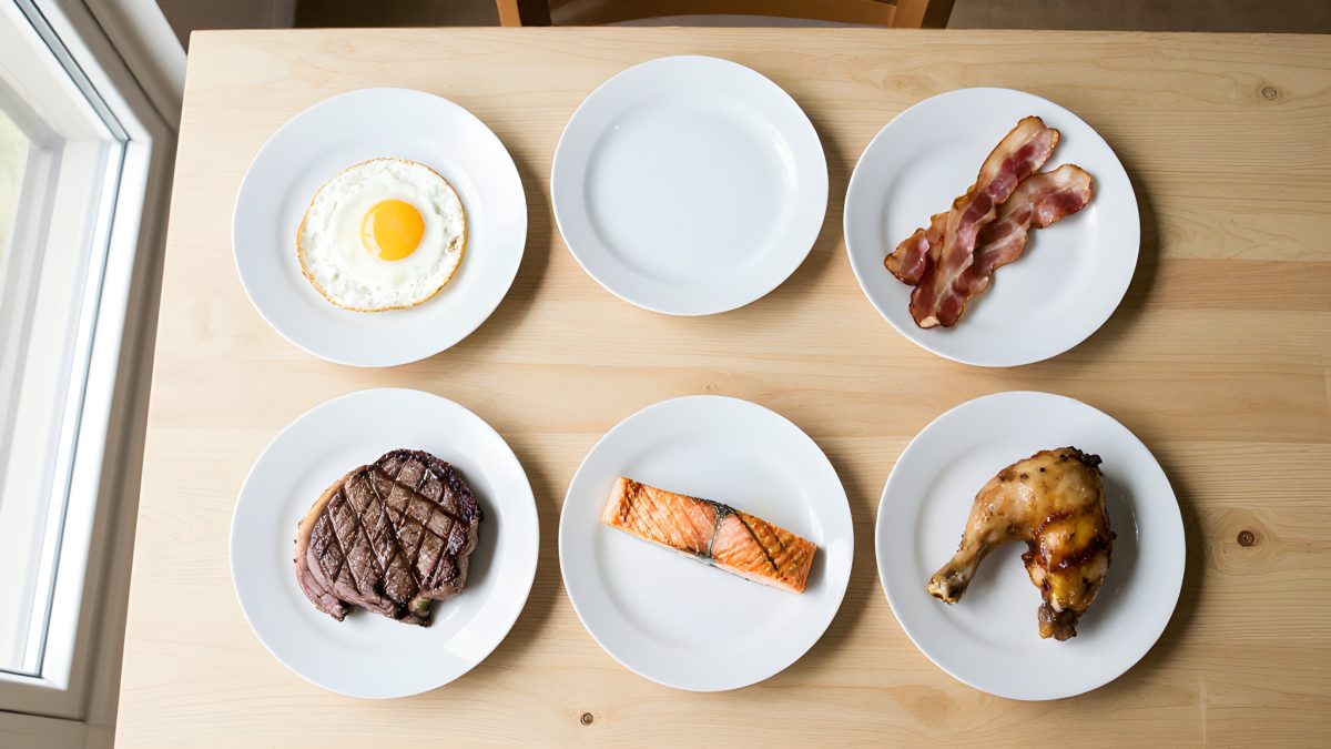 Flat-lay av carnivore-mat: biff, ägg, bacon, lax och kyckling utan några växtbaserade livsmedel.